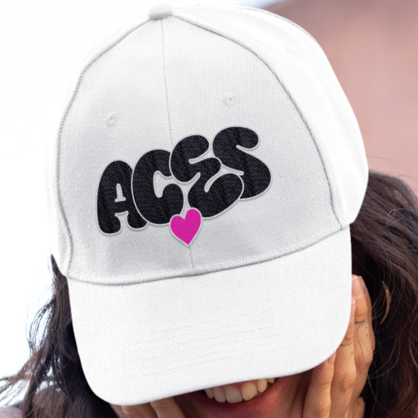 Person wearing a white cap with 'ACES' and a heart design, covering their face.