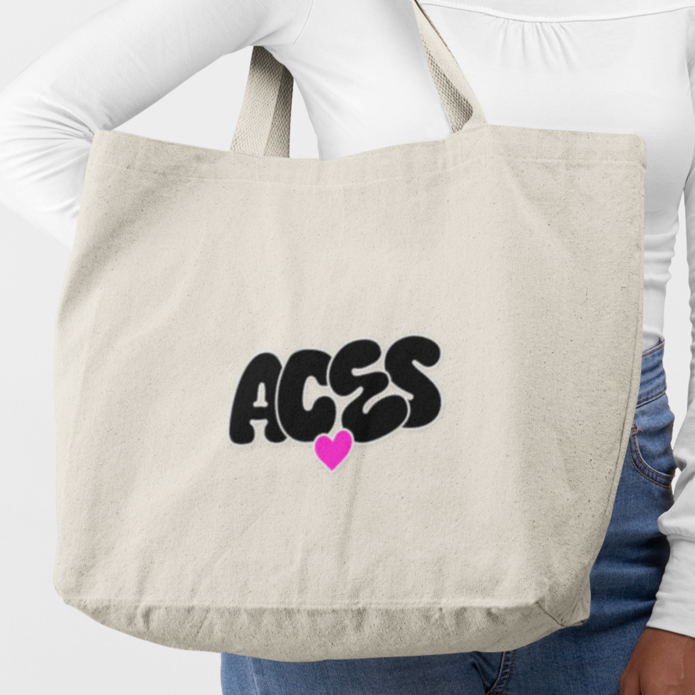Person holding a beige tote bag with 'ACES' and a heart design.