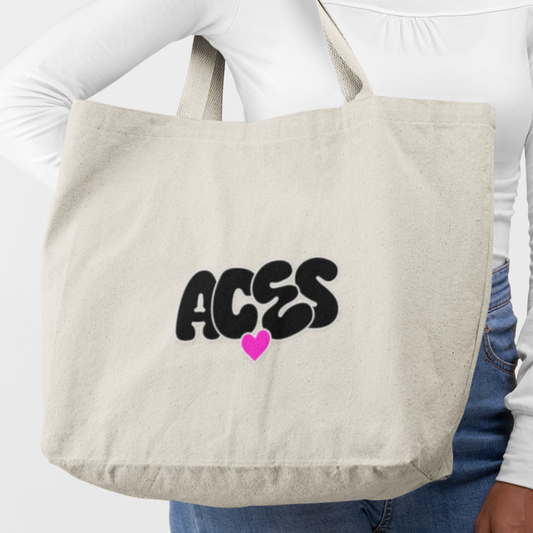 Person holding a beige tote bag with 'ACES' and a heart design.