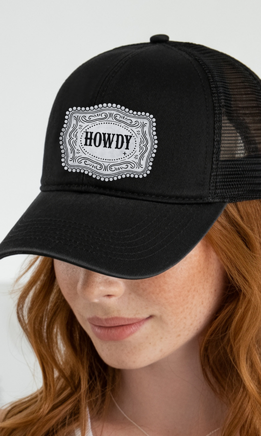Black trucker cap with 'HOWDY' patch worn by a person with red hair.
