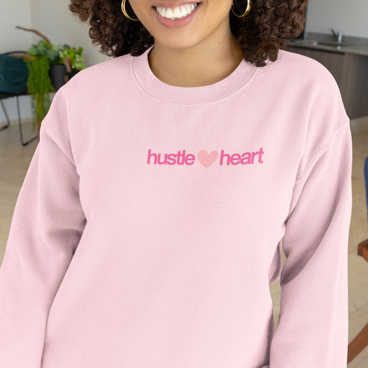 Person wearing a pink sweatshirt with 'hustle heart' text in a casual setting
