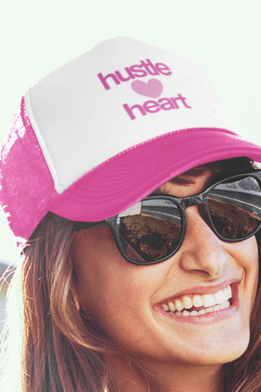 Person wearing a pink and white cap with 'hustle heart' text, smiling.