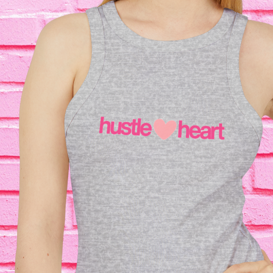 Person wearing a gray tank top with 'hustle heart' text in pink against a pink brick wall.